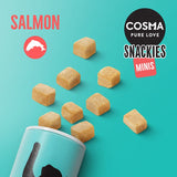 COSMA PURE LOVE SNACKIES MINIS, SALMON. Cubed treats shown spilling from a turquoise container with salmon icon and visible product name text.