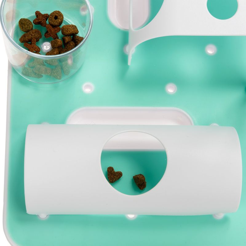 Feeding toy with green base, transparent container and white tube. Heart-shaped dry food pieces visible.