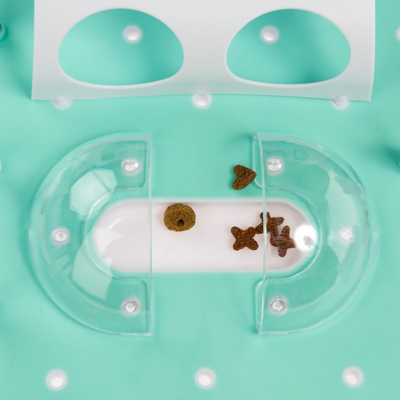 Feeding toy with transparent plastic covers and various dry food pieces on a mint green surface.