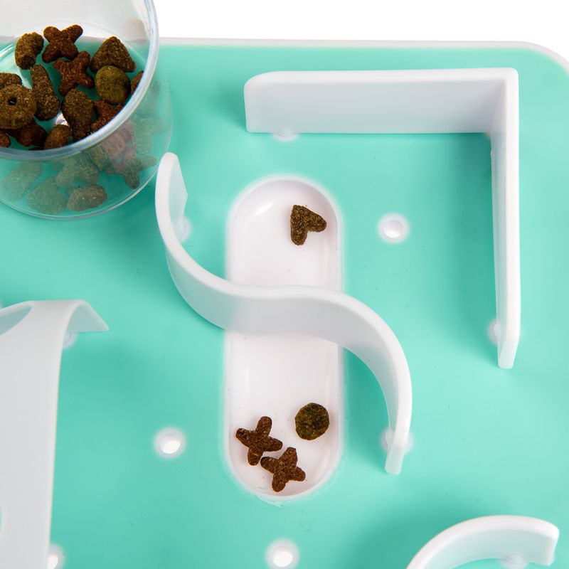 Interactive feeding toy with labyrinth design, green base and white obstacles. Dry food pieces in various shapes visible.