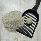 Cat litter scoop with clumps and litter on wooden surface, showing the scoop's function for cleaning cat litter.