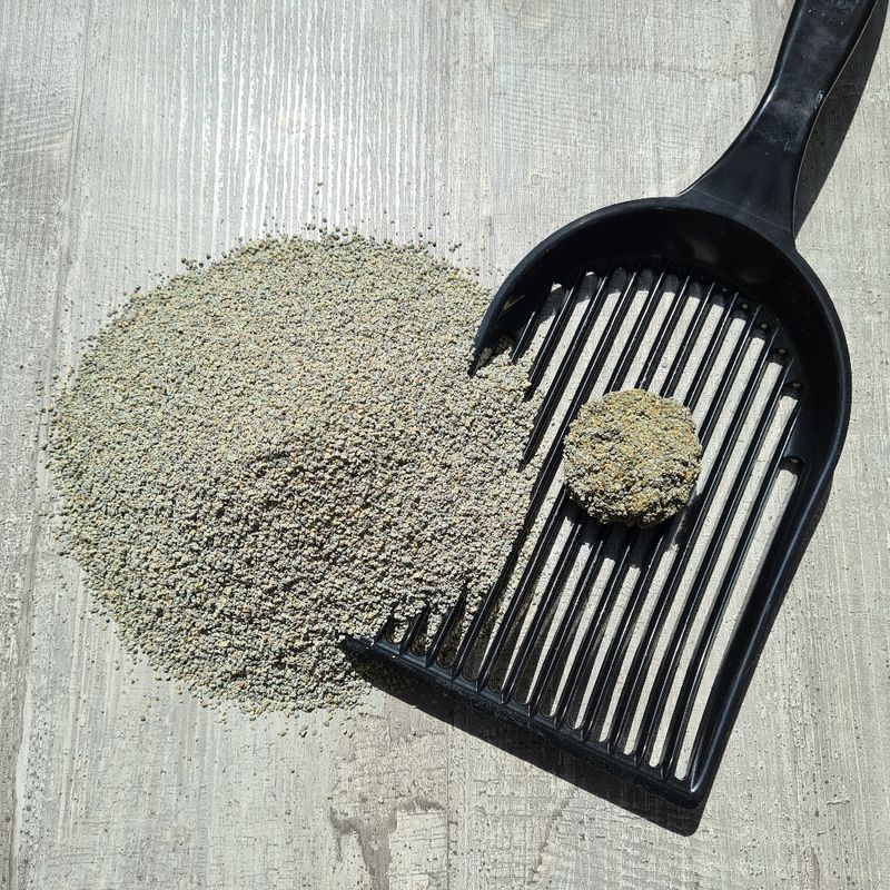 Cat litter scoop with clumps and litter on wooden surface, showing the scoop's function for cleaning cat litter.