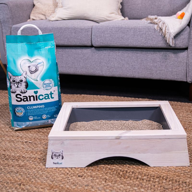Sanicat Clumping cat litter with Oxygen Control, 10L bag next to a wooden cat toilet with grey tray. Product for odour-free and hygienic cat care.