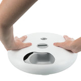 Trixie automatic feeder with digital display, two hands pressing the top for operation.