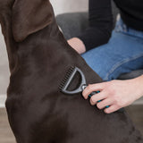 Person grooming a dog's coat with a black grooming tool. Focus on the use of the tool for coat care.