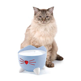 Blue cat bowl with cat ear design and red heart motif, filled with milk. Cat sitting in the background.