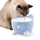 Cat drinking from a blue water fountain with cat motif and running water.