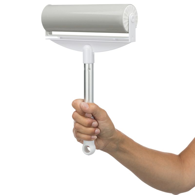 Hand holding a lint roller with silver handle and white frame, suitable for removing pet hair.