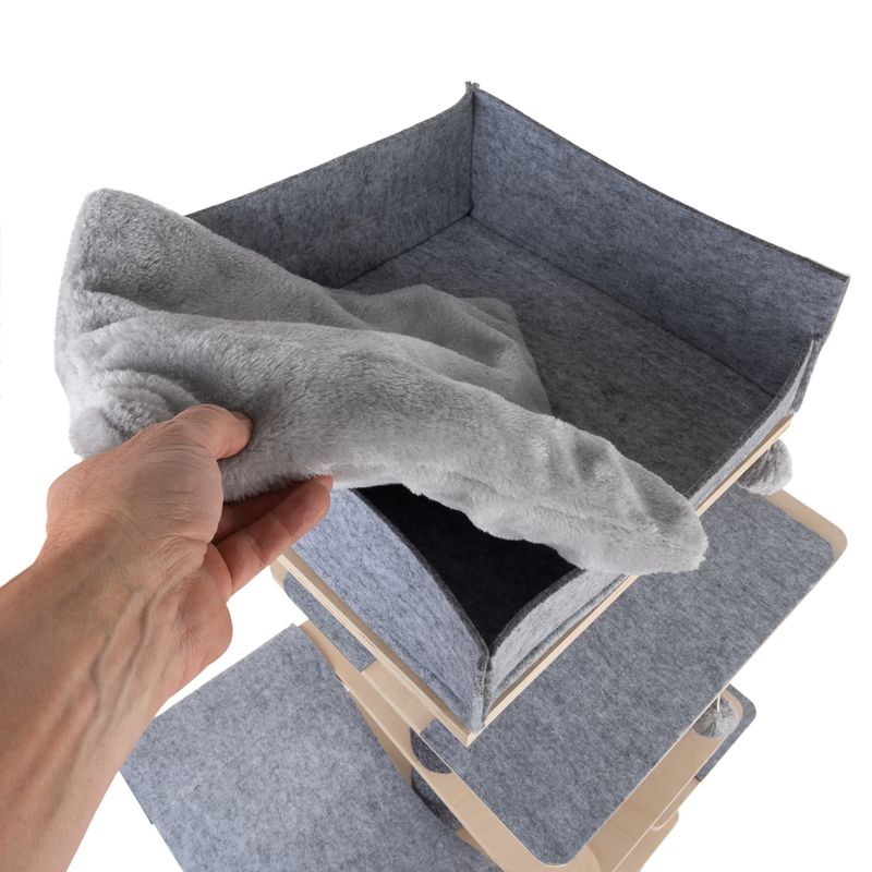 Hand places a grey, soft blanket into a square felt compartment of a multi-level wooden shelf.