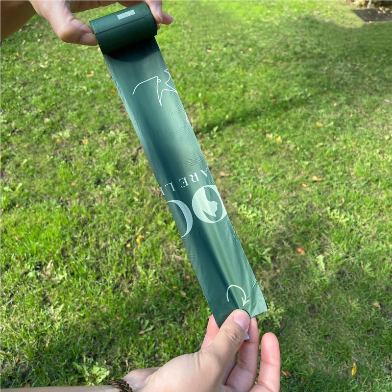 Green dog waste bag roll with white print, held by a hand. Text on bags: 'Care'.