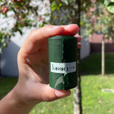kooa. Dark green roll held in one hand, with kooa logo and arrow on it.