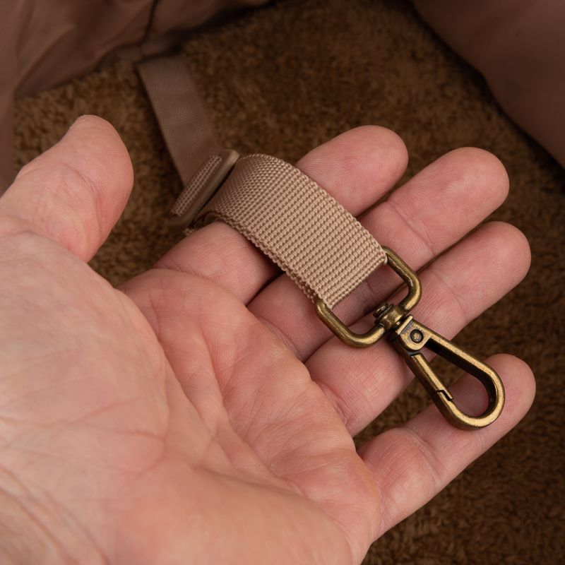 Beige nylon strap with metal carabiner hook, held in one hand. Close-up of the fastening element.