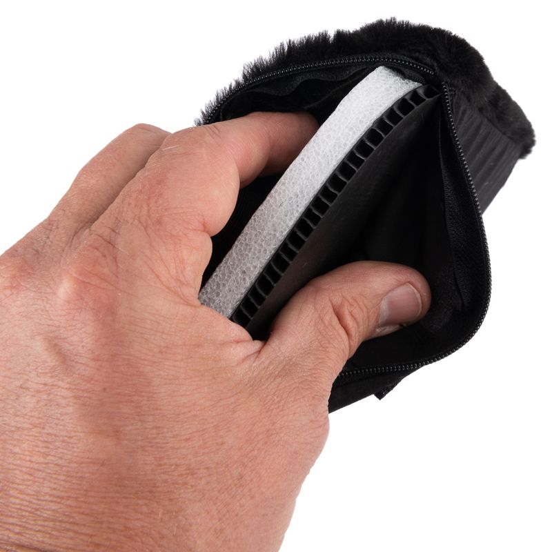 Hand holding a black product with zip, showing a white and black layer of plastic and foam.