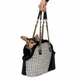 Carrier bag with black and white pattern and gold chain handles, dog sitting inside. Hand holding the bag.
