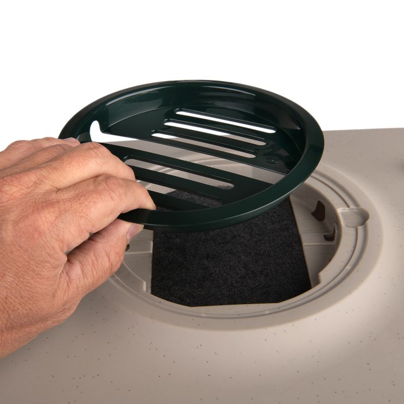 Hand lifts green lid from a round filter insert, visible is a black activated carbon filter in a beige-coloured device.