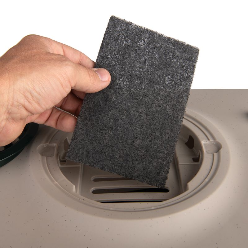 Hand holding a rectangular black filter over a round vent, showing the filter replacement process.