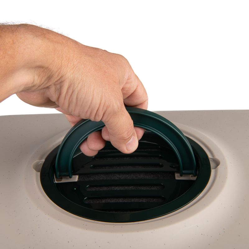 Hand holding a green handle on a ventilated lid, likely part of a carrier or box.