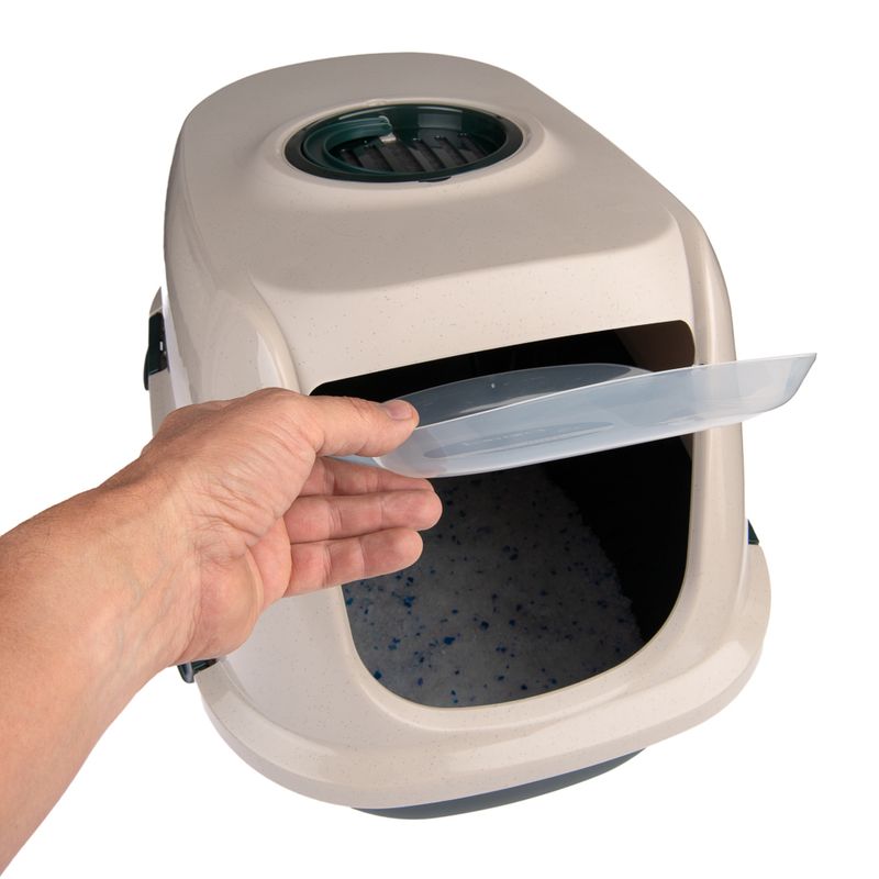 Hand opens the lid of a beige cat toilet with filter insert and visible litter inside.