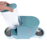 Feeding station with two stainless steel bowls and removable transparent container, suitable for dry food or water. Hand shows removal of the container.