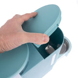 Hand opens a turquoise food dispenser with integrated metal bowl.