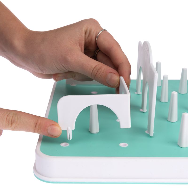 Hand showing how a white obstacle is attached to a turquoise game board. Instructions for assembling an interactive game.
