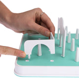 Hand showing how a white obstacle is attached to a turquoise game board. Instructions for assembling an interactive game.
