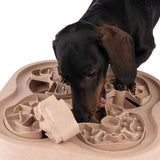 Dog interacting with a beige plastic intelligence toy featuring multiple compartments and mazes for snacks.