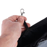 Close-up of a hand holding a metal carabiner on a black fabric strap. Detailed view of a locking mechanism.