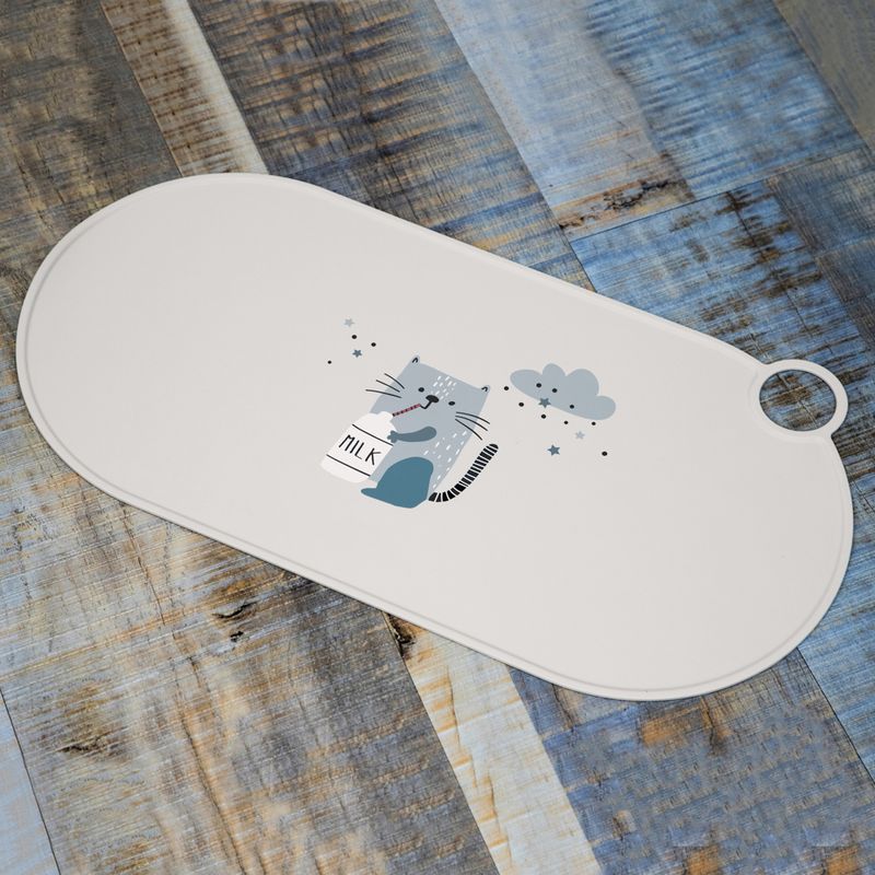 White feeding mat with cat motif, milk bottle and cloud on wooden surface.
