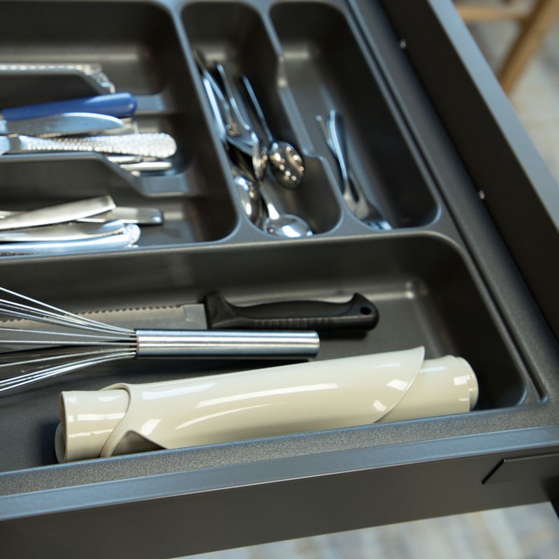 Cutlery and kitchen utensils in a grey drawer insert, including knives, a whisk, and a white handle attachment.