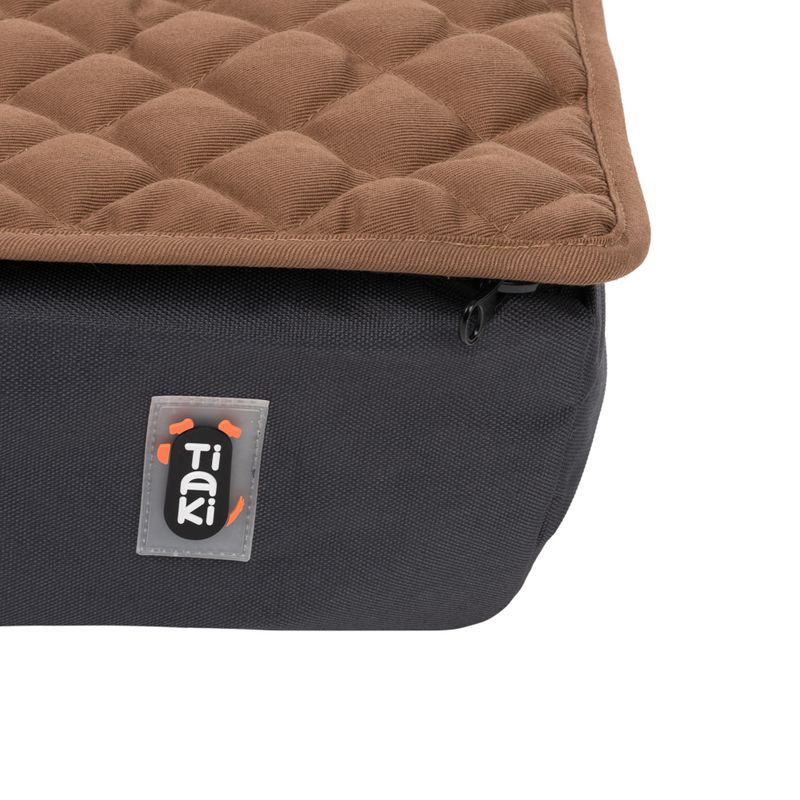 Tiaki dog bed with brown quilted surface and black fabric base. Visible Tiaki logo on the side.