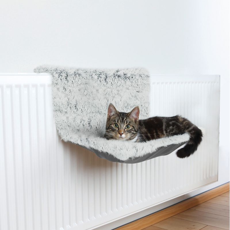 Cat bed with soft, grey cover attached to a radiator. A tabby cat is lying relaxed on it.