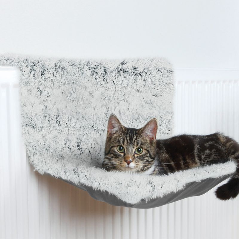 Cat bed made of grey plush, attached to a radiator. Tabby cat lying relaxed on it.