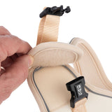 Close-up of a beige dog harness with padded hook-and-loop fastener and black plastic buckle. Hand shows the opening of the fastener.