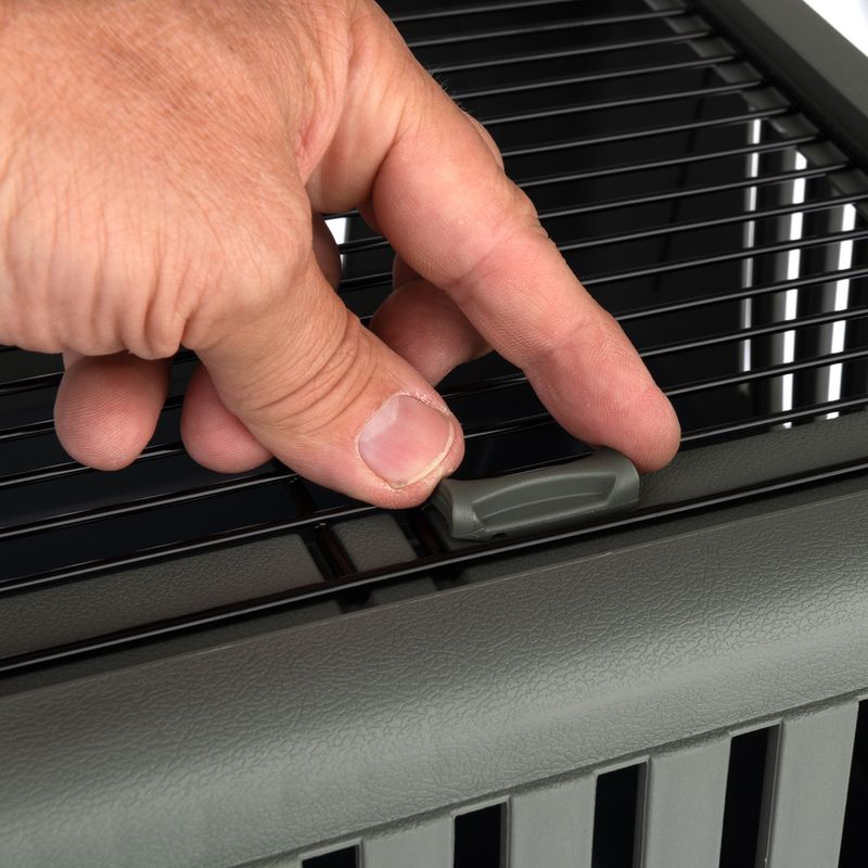 Hand showing how the locking mechanism of a grey transport cage is opened.