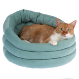 Cat bed in light green with an orange and white cat lying inside. Round design with padded edges.