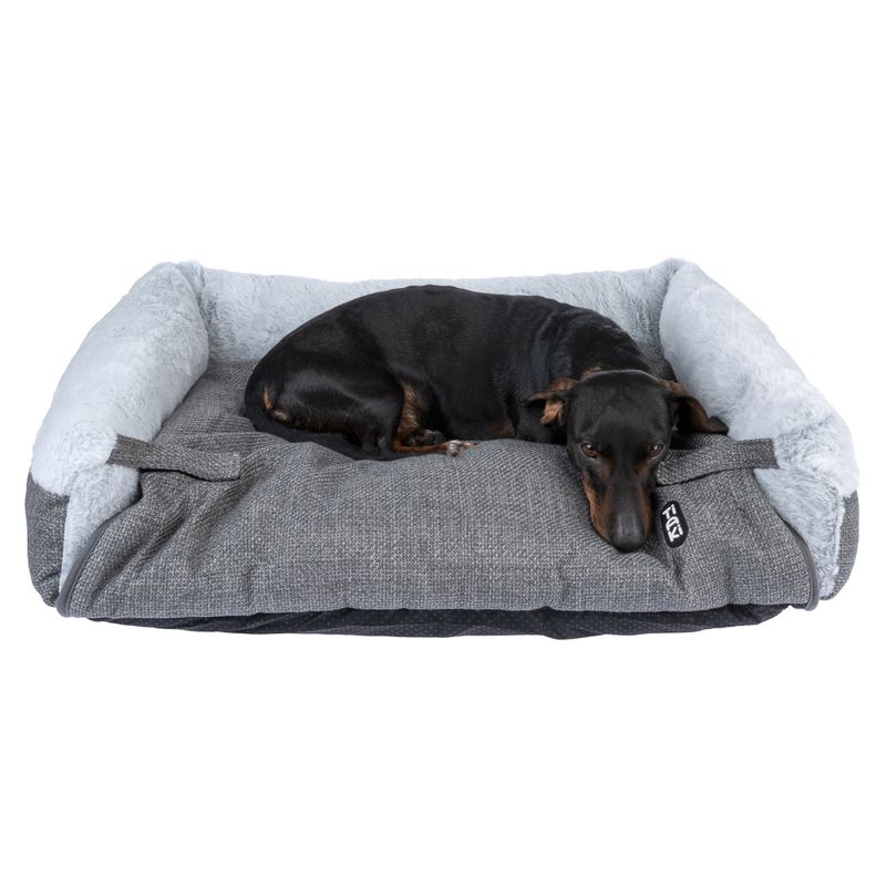 Black dog lying on a grey dog bed with a soft, light grey edge and visible TIAKI logo.