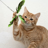 Red cat playing with a cat toy made of green feathers and a wooden bead on a string.