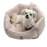 Dog sitting in a beige, fluffy dog bed with Tiaki logo on the front.