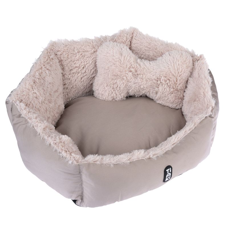 Round, beige pet bed with soft plush edge and matching bone-shaped cushion. 'Tia' brand logo visible on the outside.