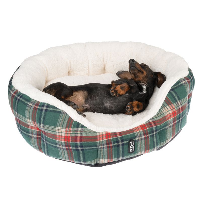 Dog sleeping in a soft, checked dog bed with white inner lining. Trixie brand logo visible on the outside of the bed.