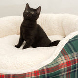 Black cat sitting in a white, fluffy pet bed with a checked border.