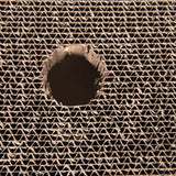 Close-up of corrugated cardboard with a round hole in the centre, showing the material's structure.