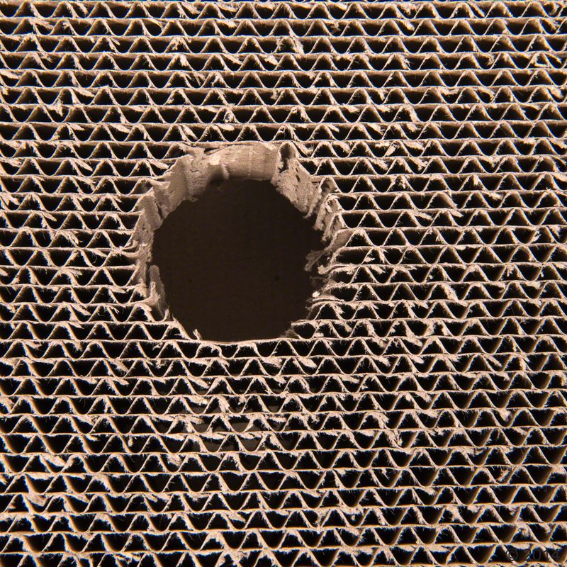 Close-up of corrugated cardboard with a round hole in the centre, showing the material's structure.