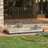 Large cage with metal grid walls and plastic base, equipped with hay rack and water bottle. Suitable for outdoor use, shown on a terrace with grass area.