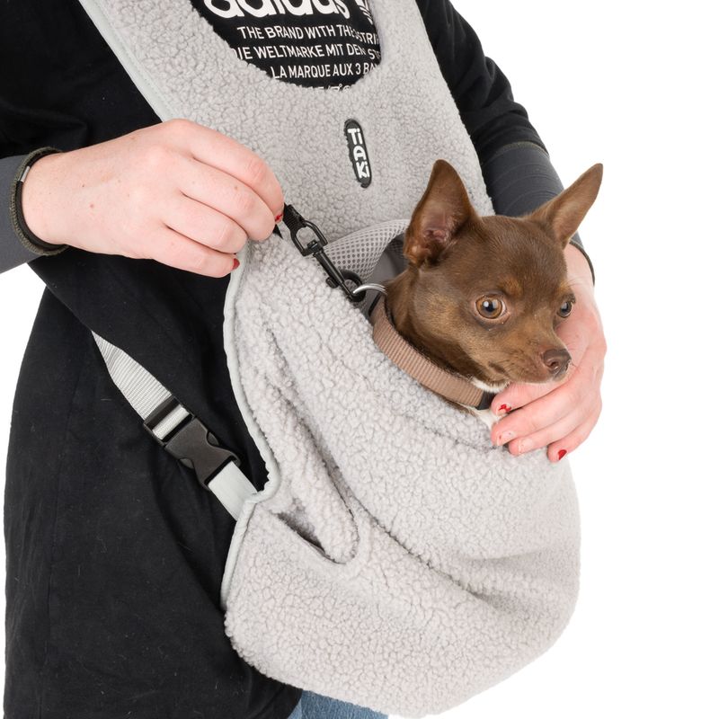 Carrier bag made of grey fleece with safety clip, suitable for small dogs. Dog sits securely in the bag while person holds the clip attachment.