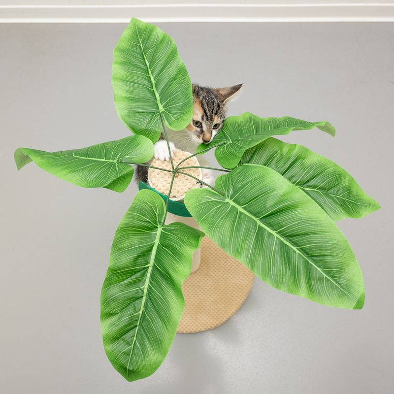 Cat tree with large artificial green leaves and sisal trunk, cat playing on it.