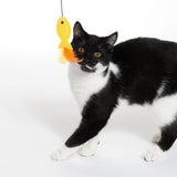 Black and white cat playing with yellow fish toy with orange feathers on a string.