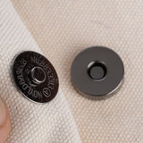 Close-up of a metal magnetic clasp on beige fabric, consisting of two parts: one with a raised centre and one flat disc.