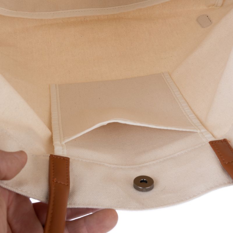 Interior view of a beige fabric bag with brown handles, small inner pocket and magnetic closure.